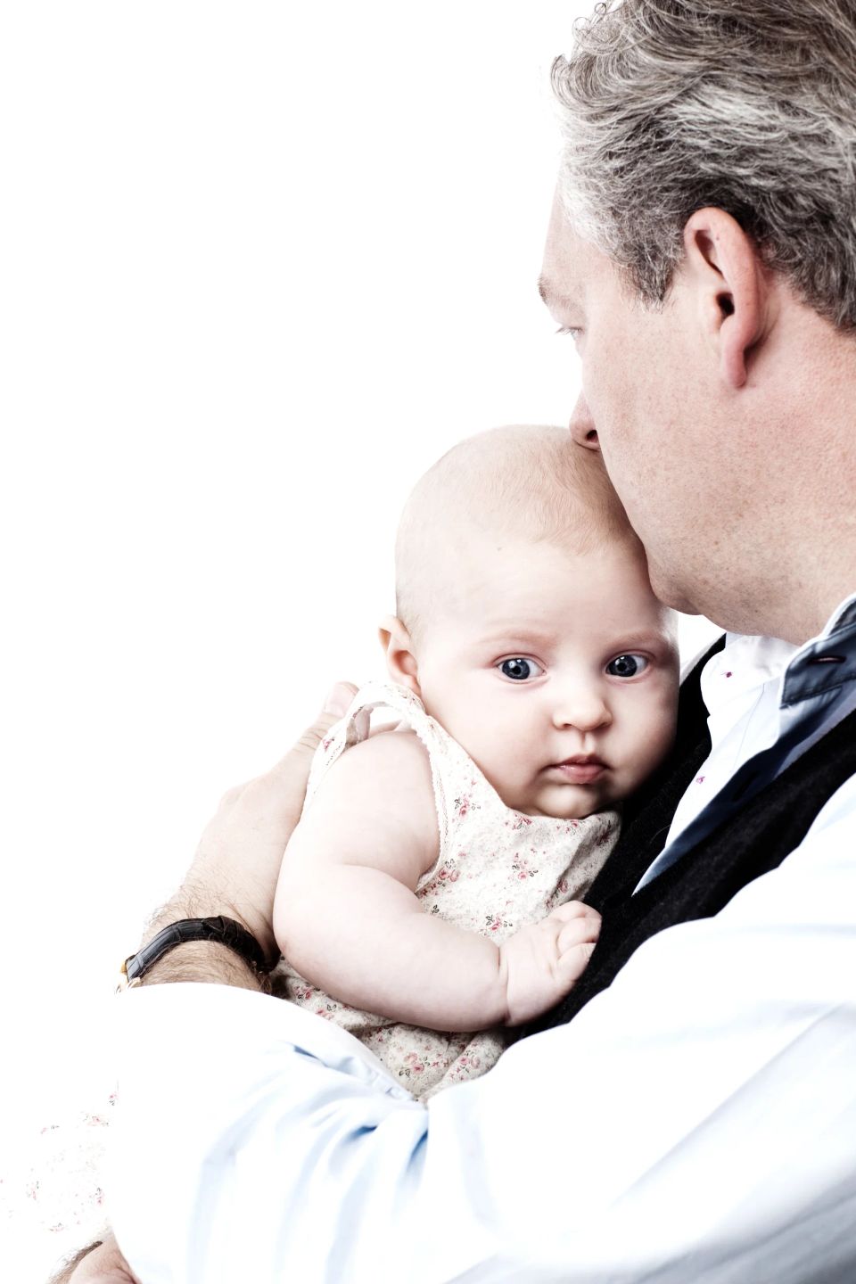 Familiefotografering: Far kysser sin baby på panden. Baby kigger nysgerrigt frem med åbne øjne, lyst og rent udtryk.