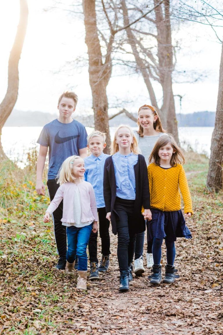 Familiefotografering: Seks glade børn i forskellige aldre går hånd i hånd på en sti ved søen i Virum.