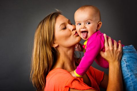 Legende baby med tungen ude og kærligt kys fra mor