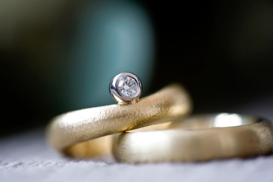 Nærbillede af et par matte guldbryllupsringe. Den ene har en skinnende diamant.