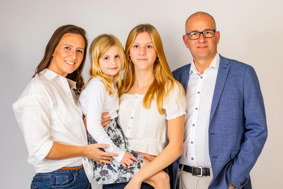 Familiefotografering: Smilende familie på fire i hvidt studie. Forældre med to piger, en teenagedatter og et mindre barn.
