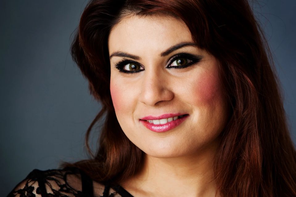 Nærbillede af smilende kvinde med mørkt hår, intenst øjenblik og pink læbestift, let makeup og mørk overdel. Portrætfoto.