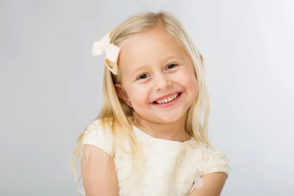 Nærbillede af legende barn med smil, langt blond hår og lysegul sløjfe, lyse farver. Kategorien er børn.