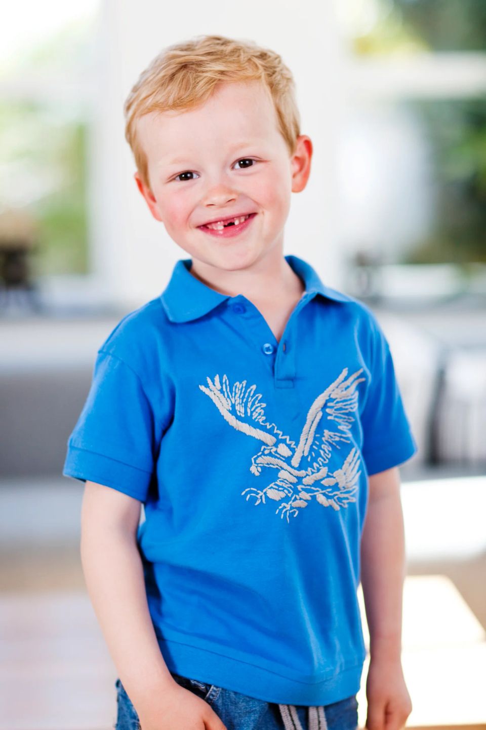 Nærbillede af et smilende barn i en blå t-shirt med manglende fortand, der skaber et kært børnefoto.