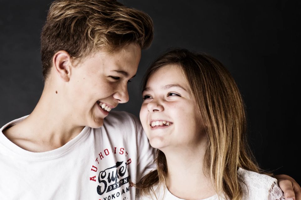 Børn: To glade teenagere med brune hår, der smiler til hinanden mod en mørk baggrund i et autentisk foto.