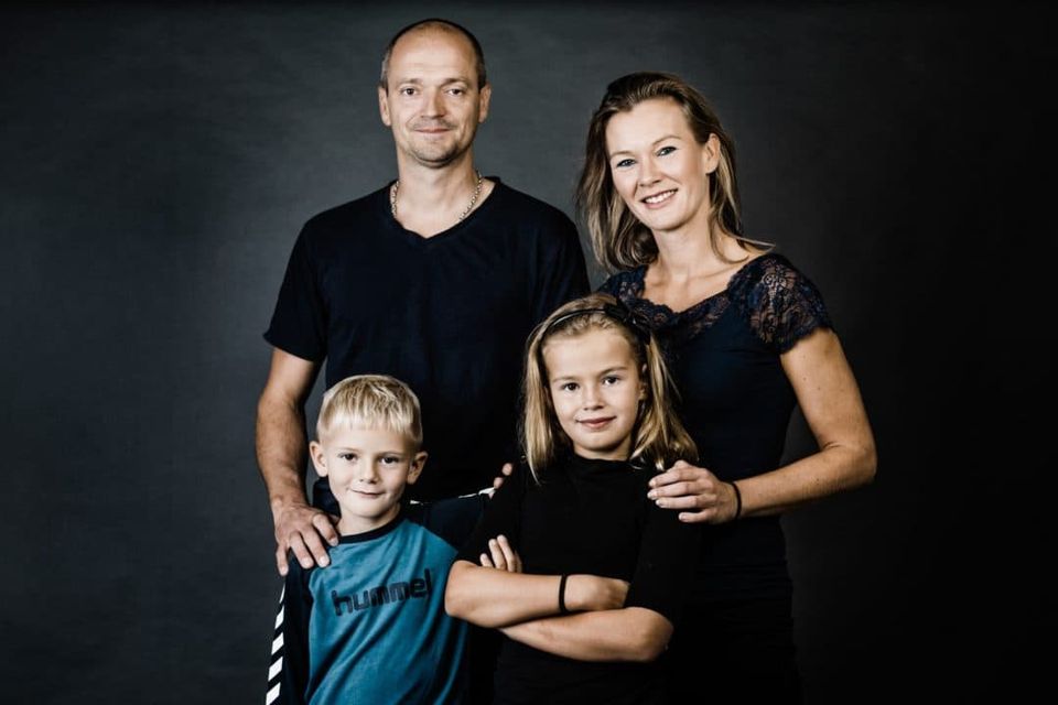 Familiefoto af forældre med deres to børn stående foran en grå baggrund. Børnene er ca. 5 og 8 år gamle.