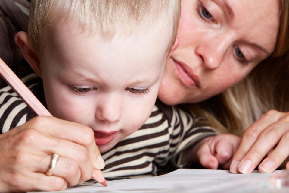 Et familiefoto af en mor og hendes lille barn, der tegner sammen. Barnet holder en farveblyant med koncentreret udtryk.