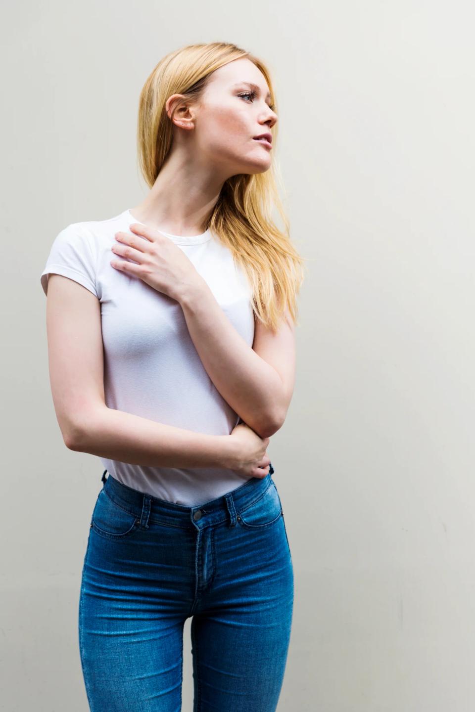 Portrætfoto af smuk, lyshåret kvinde i hvid T-shirt og jeans, der kigger opmærksomt mod højre med blødt lys.