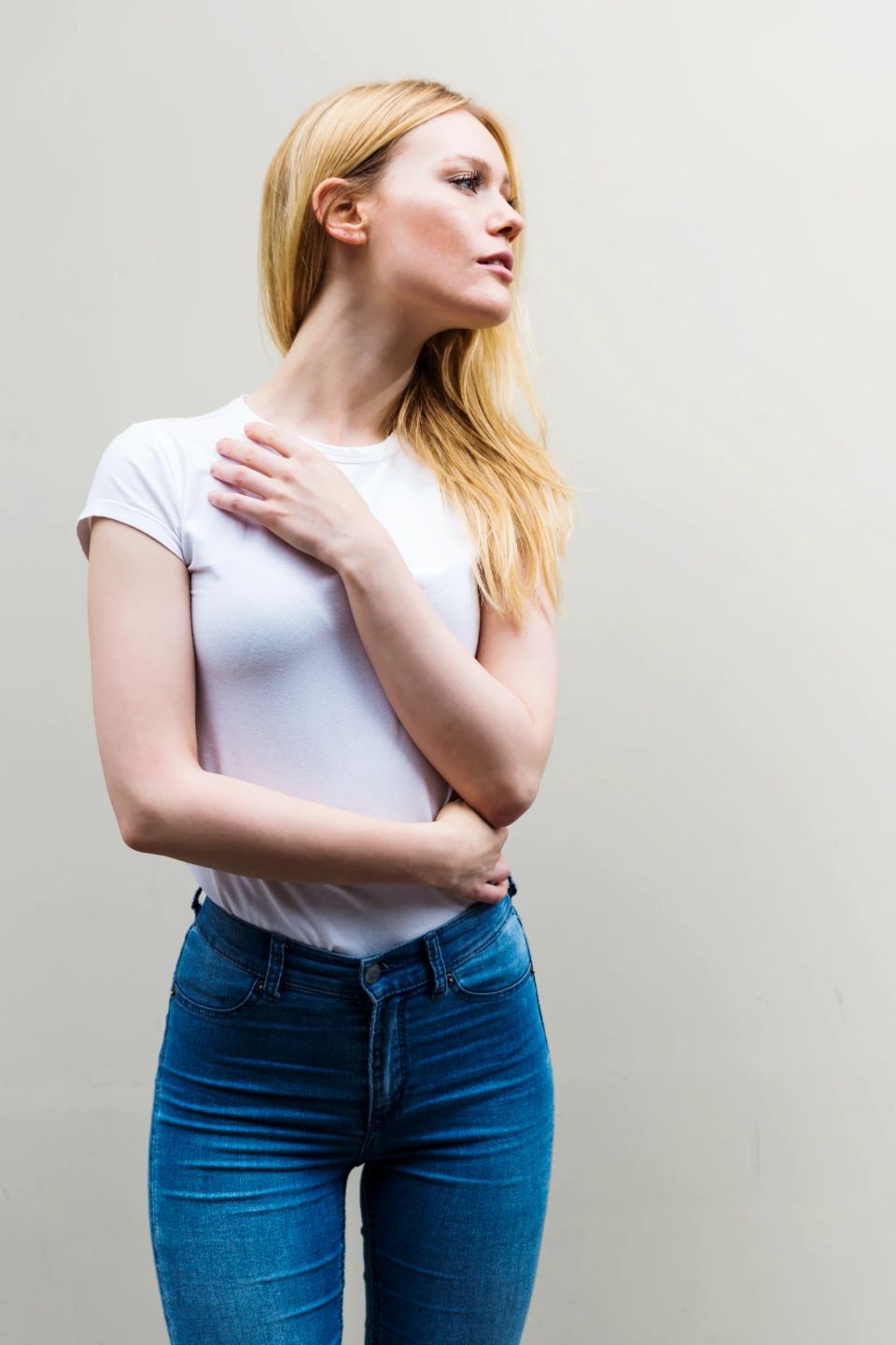 Portrætfoto af smuk, lyshåret kvinde i hvid T-shirt og jeans, der kigger opmærksomt mod højre med blødt lys.