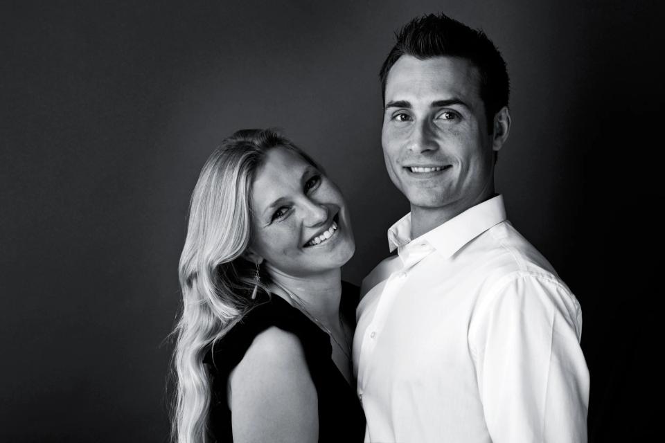 Professionelt sort-hvid portrætfoto af et smilende par, der står tæt med mørk baggrund og blødt lys.