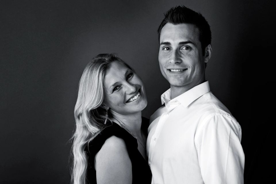 Professionelt sort-hvid portrætfoto af et smilende par, der står tæt med mørk baggrund og blødt lys.