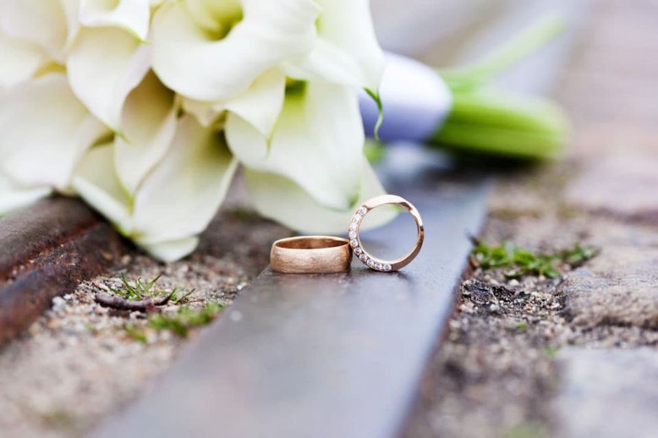 Nærbillede af to vielsesringe i rosaguld og en hvid brudebuket, der lyser op i baggrunden. Perfekt bryllupsfotografering.