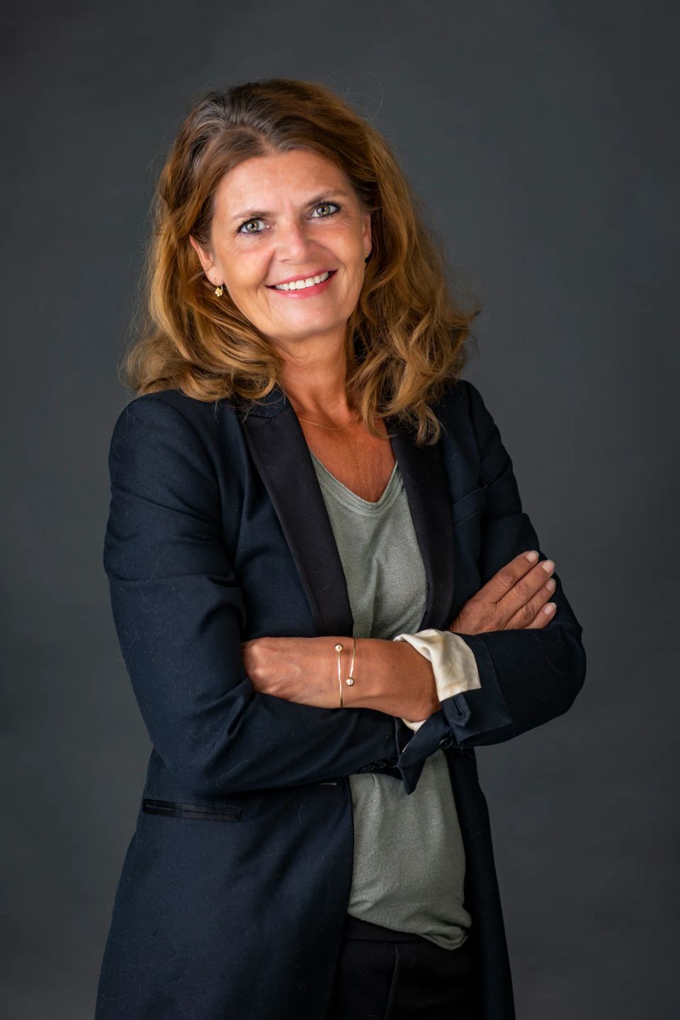 Portrætfoto af smilende kvinde med lysebrunt hår og sorte øjne, iført sort jakke og grå bluse.