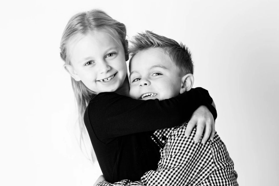 Sort-hvidt børnefotografi af søskendekram. En pige krammer sin smilende lillebror tæt. Ægte følelser fra børnene.