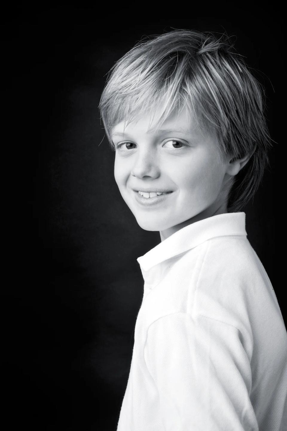 Nærbillede af et smilende barn med lyst hår, der kigger op, i et sort-hvid studieportræt. En del af min børnefotografering.