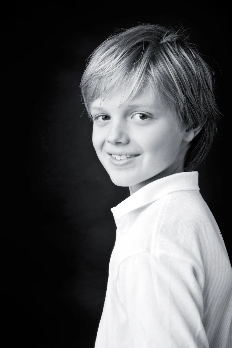 Nærbillede af et smilende barn med lyst hår, der kigger op, i et sort-hvid studieportræt. En del af min børnefotografering.