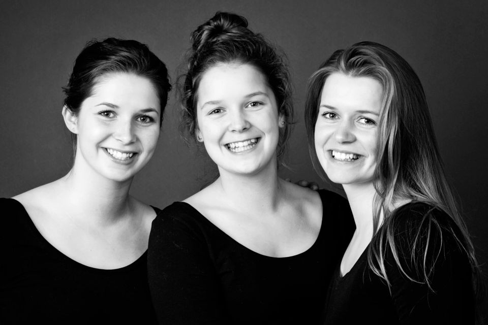 Sort-hvid familiefotografering af tre smilende søstre i sorte bluser med naturligt, varmt lys.