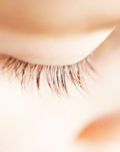 Nærbillede af et barns lukkede øje med lange øjenvipper i blødt lys, der udstråler fred og ro.