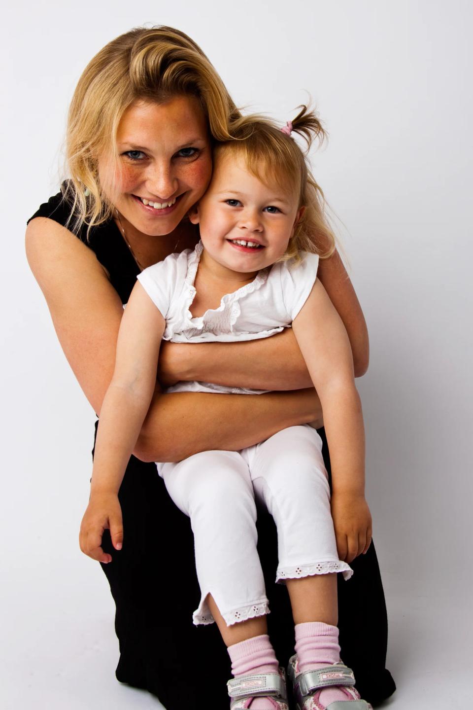Familiefoto af smilende mor og datter i autentisk sort/hvid portræt, omfavnende på en hvid baggrund.