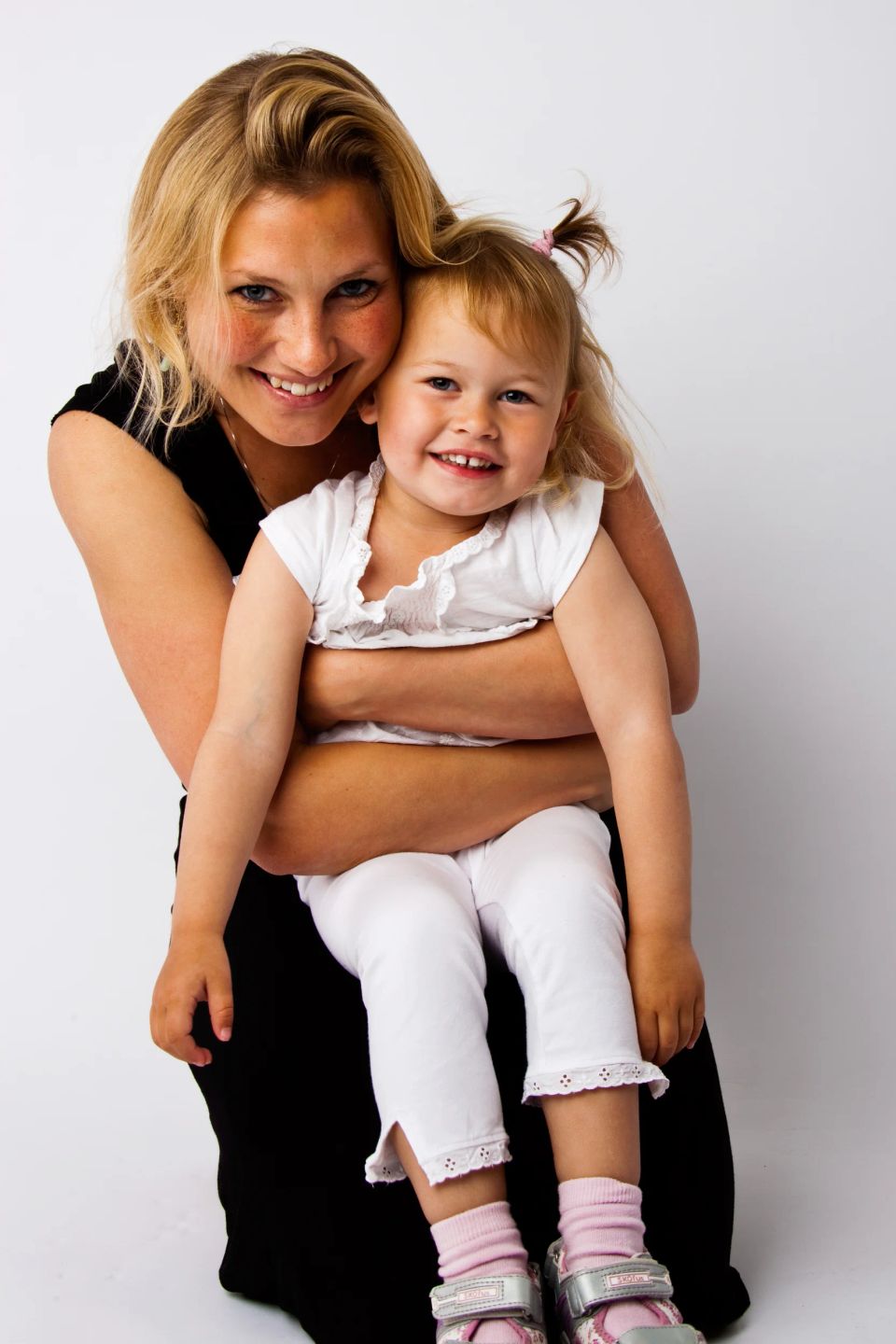 Familiefoto af smilende mor og datter i autentisk sort/hvid portræt, omfavnende på en hvid baggrund.