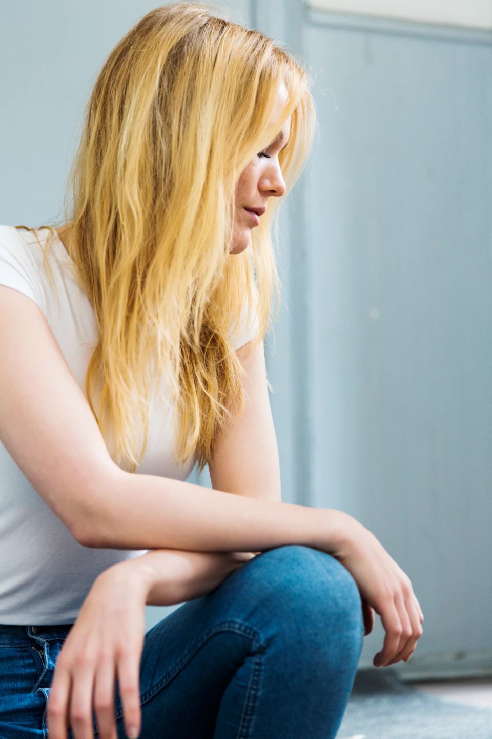 Portrætfoto af ung kvinde med langt, lyst hår, lukkede øjne og sænket hoved, i dæmpet sidelys.