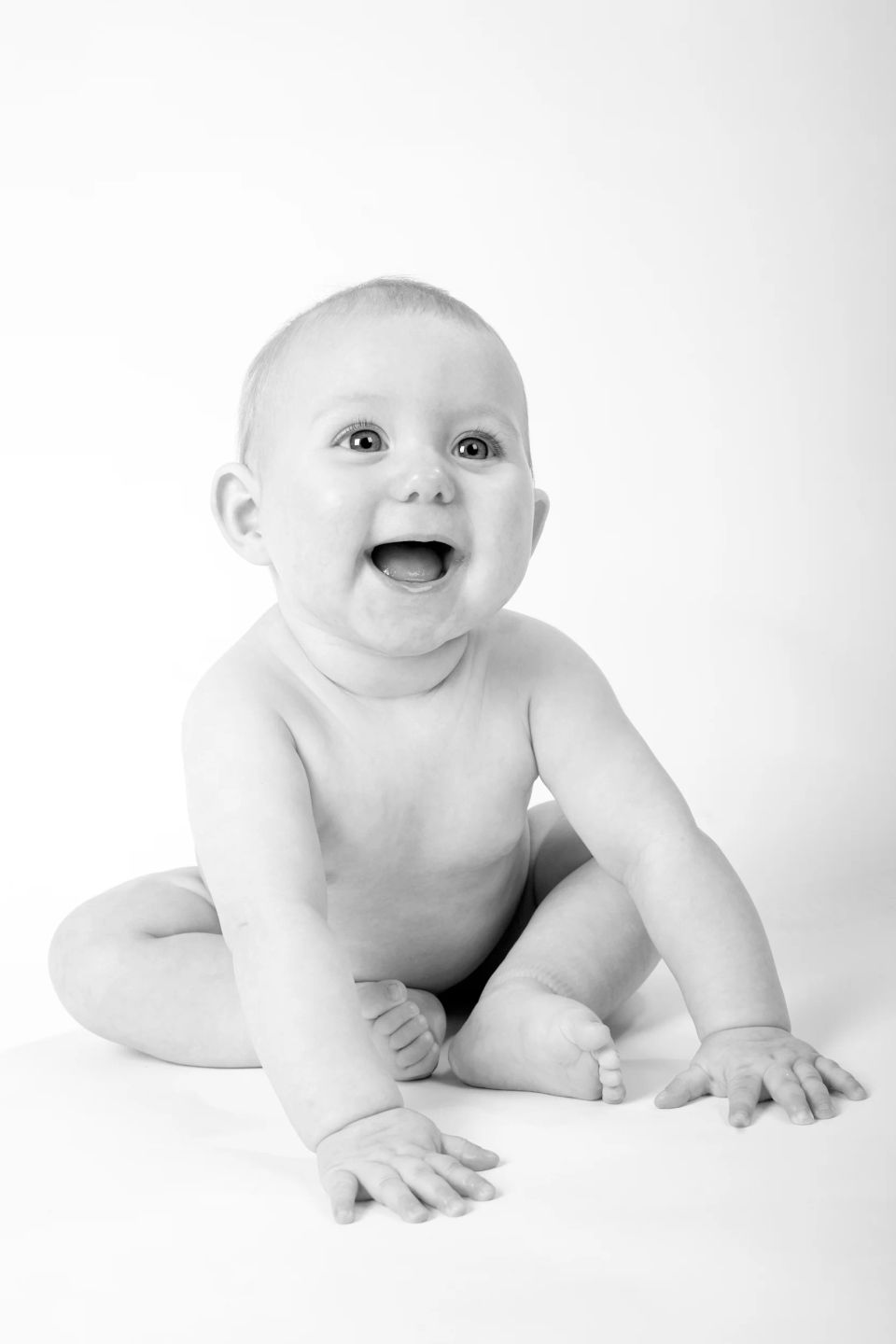 Babyfotografering af en glad baby i sort/hvid, siddende med åben mund og store øjne, lyst og rent udtryk.