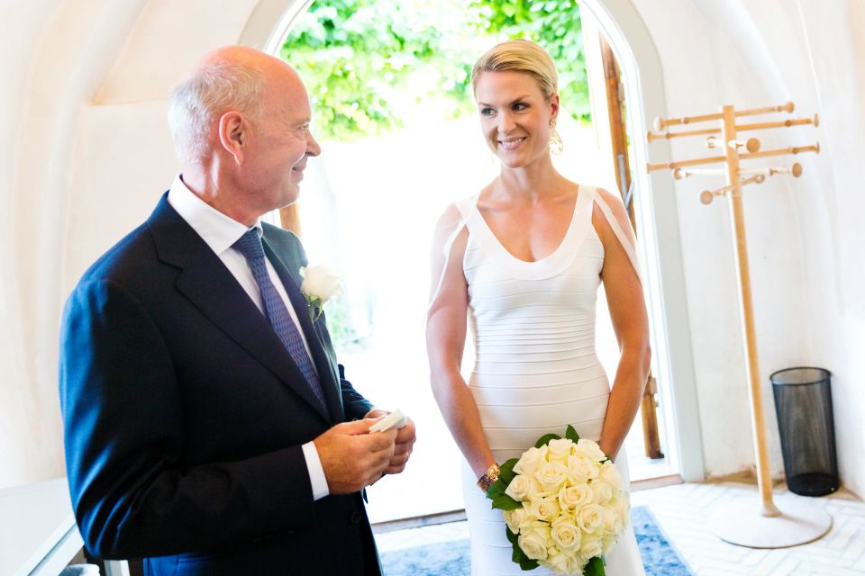 Bryllupsfoto af smilende brud med hvid brudebuket og gom i mørkt jakkesæt i Våbenhuset, klar til vielse.