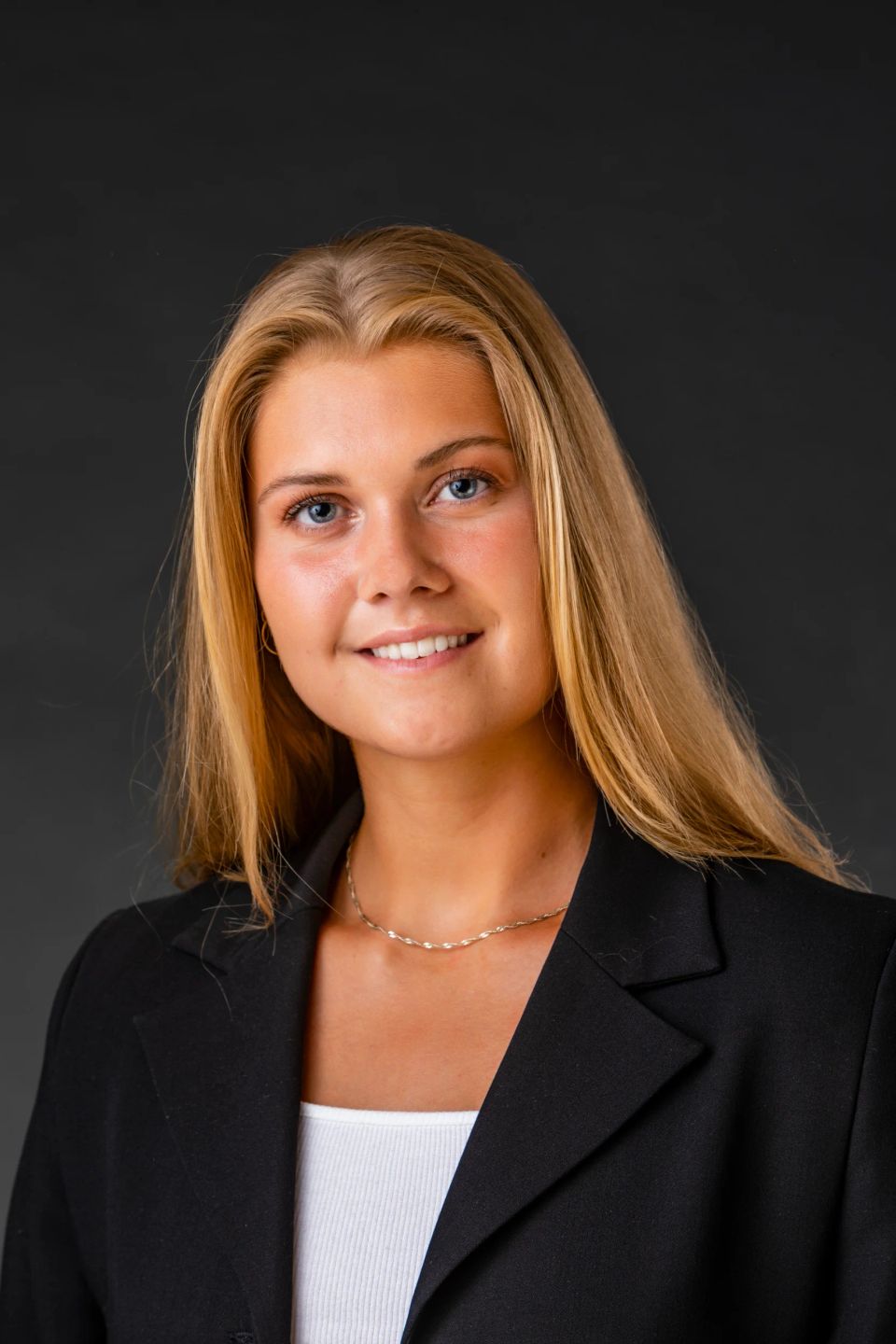 Portrætfoto af smilende ung kvinde med langt blondt hår og blå øjne i sort blazer fotograferet i studie.