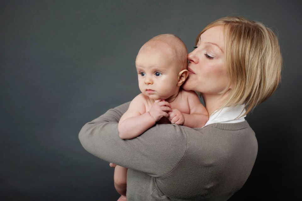 Familiefoto af mor, der kysser sin baby på kinden med lukkede øjne, autentisk og kærligt øjeblik.