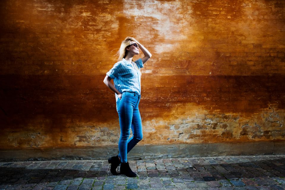 Portrætfoto af ung kvinde i jeans og skjorte, der skærmer for solen med hånden mod en rustik mur i Virum.