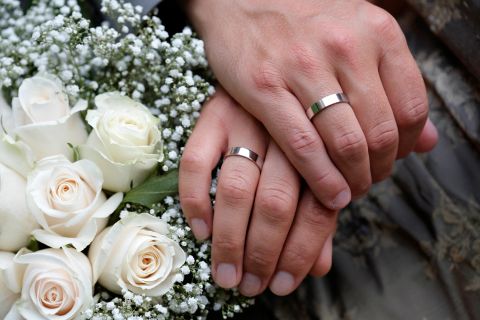 Hænder med vielsesringe og brudebuket