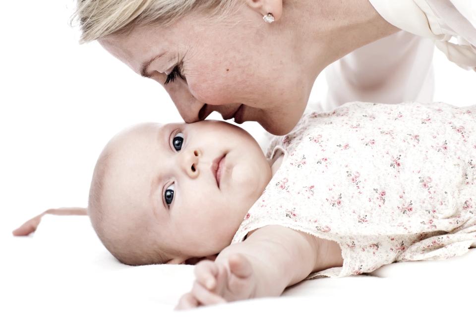 Nærbillede af babyfotografi, hvor en mor kysser sin baby på panden. Barnet ligger ned og kigger direkte mod kameraet.