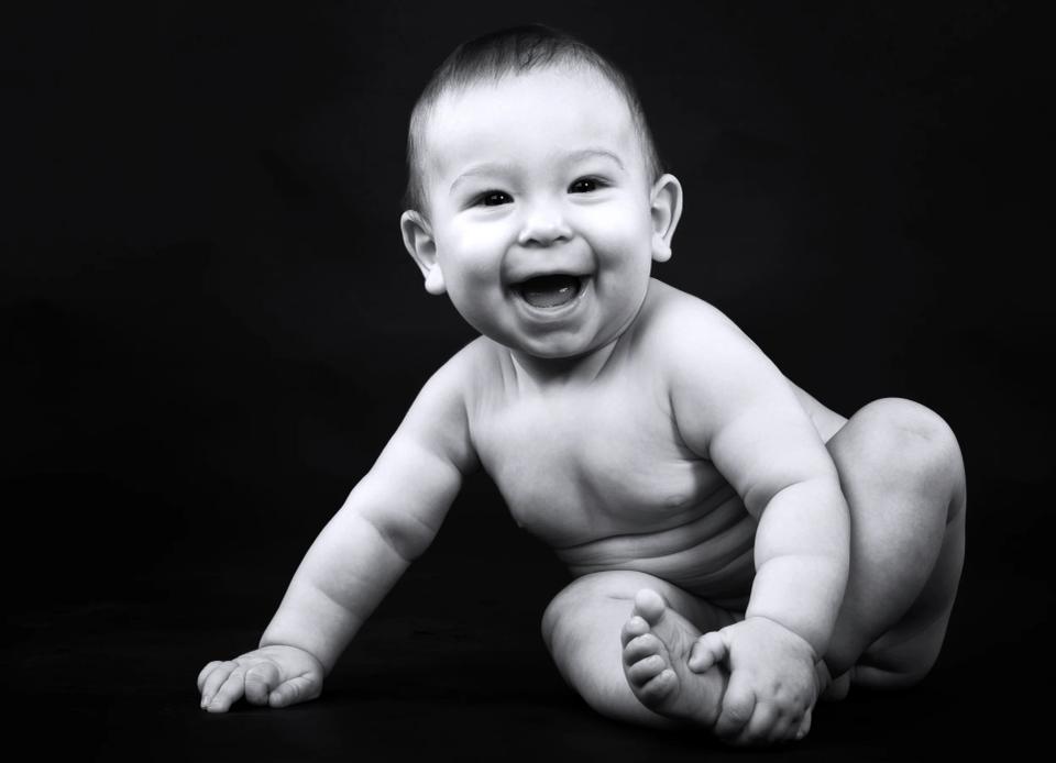 Babyfotografering: Glad baby med autentisk smil liggende på en mørk baggrund i sort/hvid