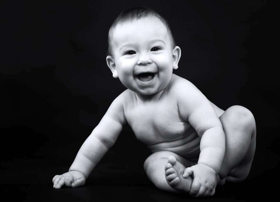 Babyfotografering: Glad baby med autentisk smil liggende på en mørk baggrund i sort/hvid