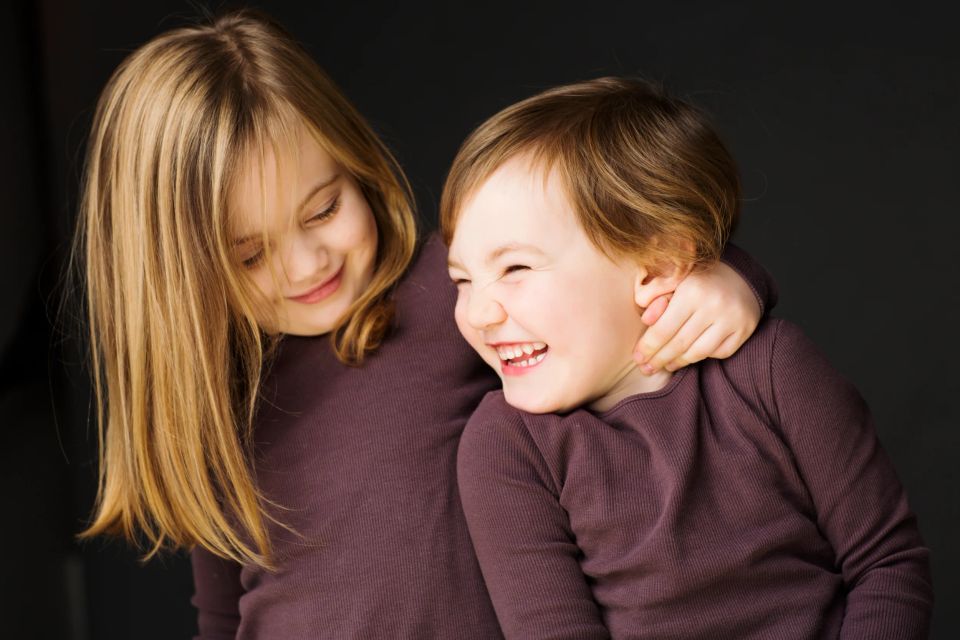 Nærbillede af to glade, grinende børn med brunt tøj, der omfavner hinanden i et legende øjeblik. Børnefotografering.