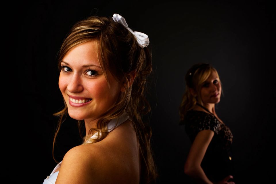 Portrætfoto af smilende kvinde i hvid top, med en anden kvinde i baggrunden, begge med mørk baggrund.