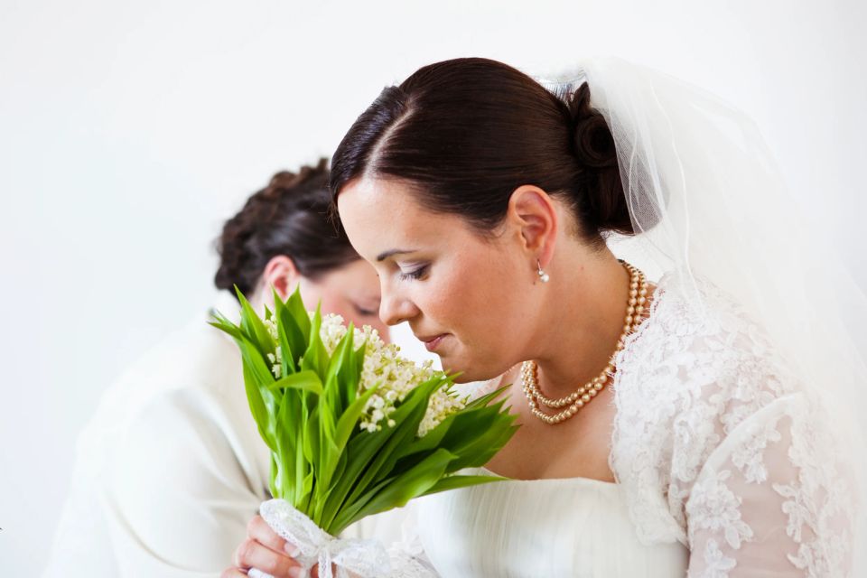 Brud i hvid blondekjole og slør dufter til en markant, grøn brudebuket med hvide blomster. Bryllupsfotografi.