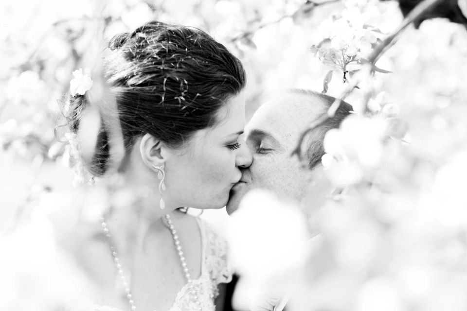 Bryllupsbillede: Brudepar kysser omgivet af lyse blomster. En romantisk, blød stemning i sort/hvid