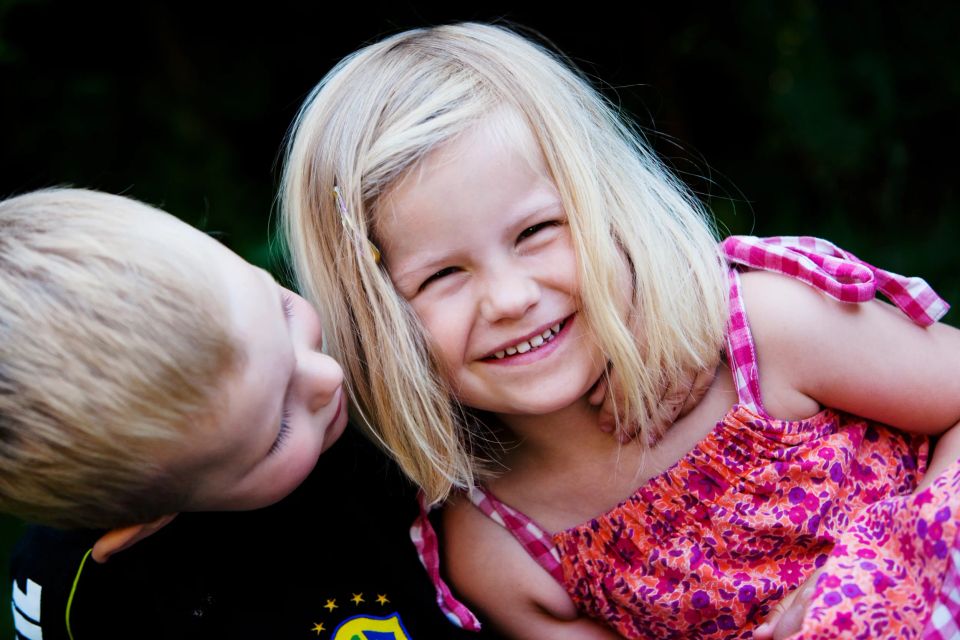 Billede af to glade børn der leger. En pige med lyst hår smiler stort, med et barn hvis hoved hviler mod hendes skulder.