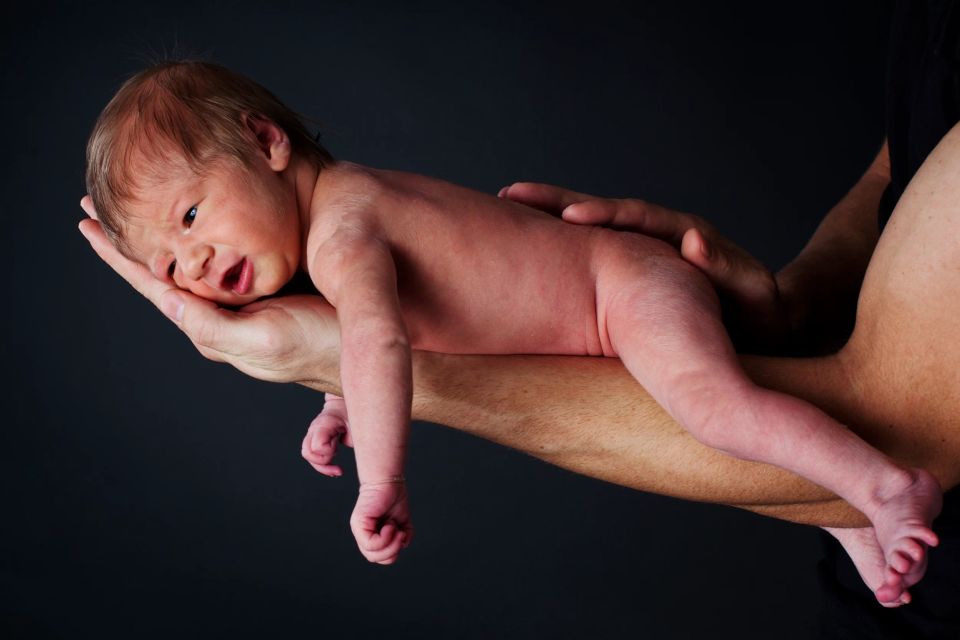 Babyfotografering i sort/hvid af en nyfødt baby liggende på en voksens hænder med mørk baggrund.