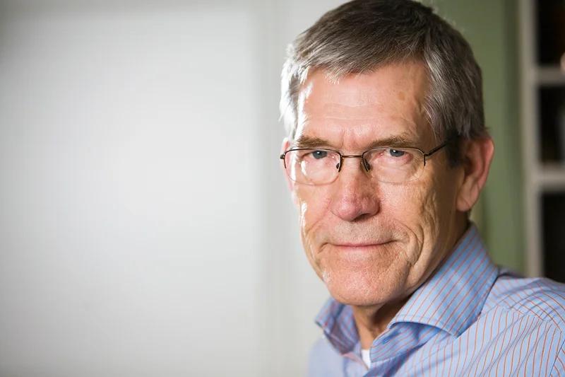 Professionelt portræt af moden mand med briller i stribet skjorte, blød belysning og neutral baggrund.