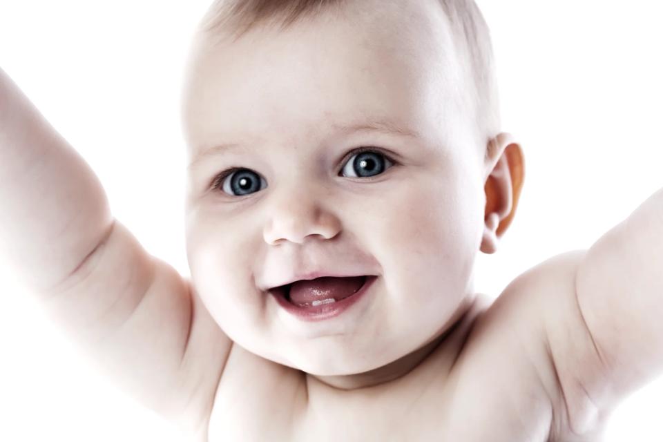 Glad baby med blå øjne og åben mund rækker armene op i en autentisk babyfotografering med hvid baggrund.