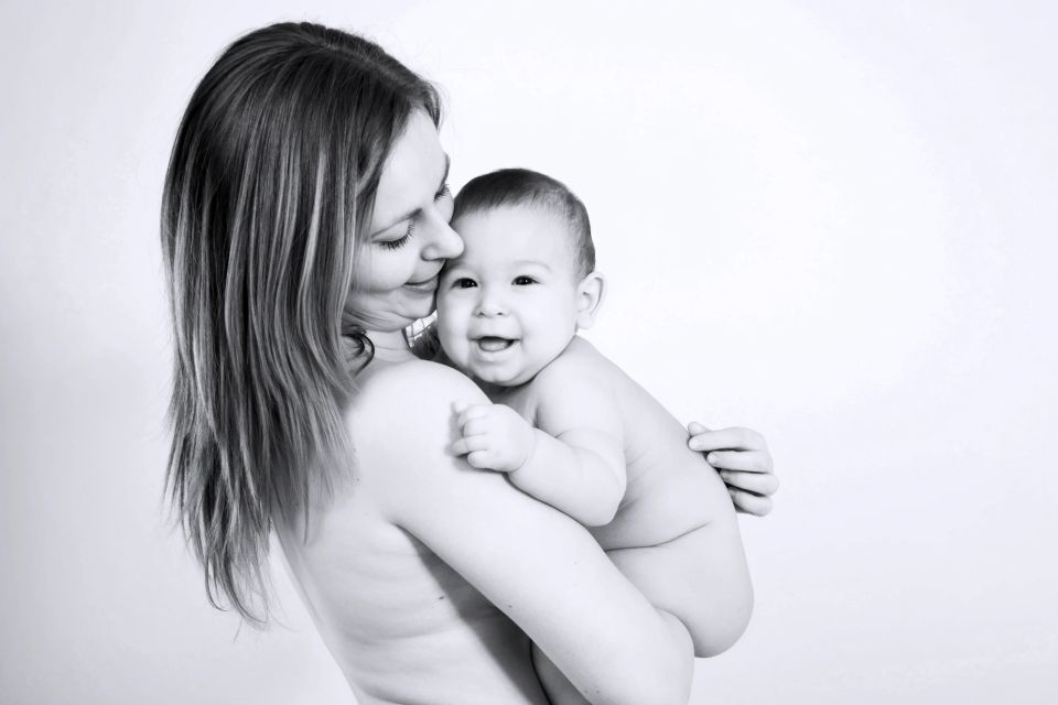 Sort/hvidt babyfotografi: En mor omfavner sin lille, glad baby der smiler. Intim og kærlig stemning.