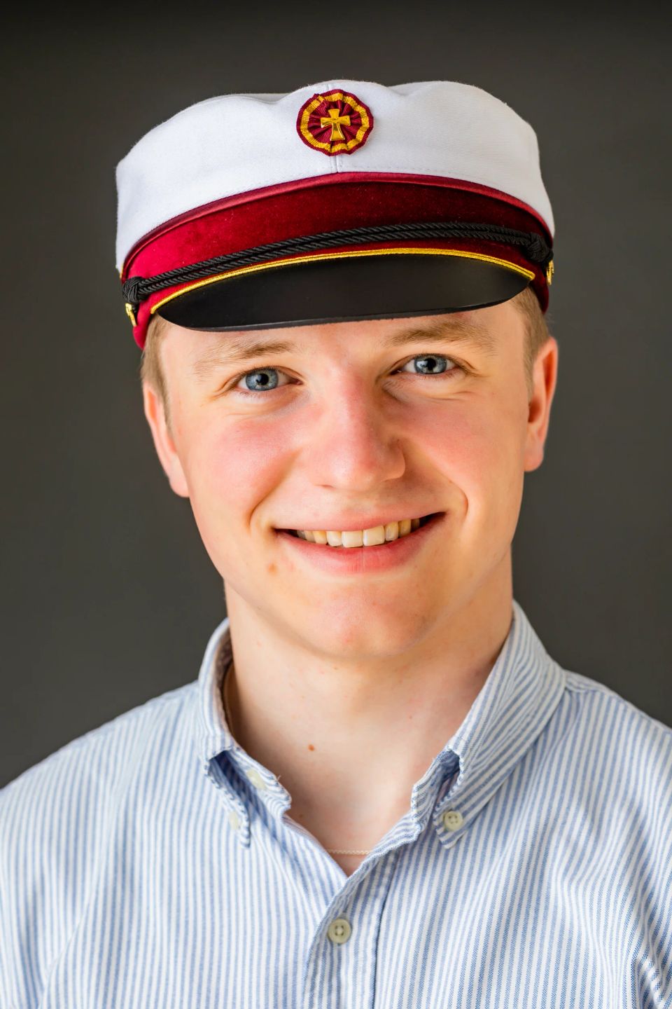 Glad ung mand i studenterhue med blåt og hvidt stribet skjorte. Et portrætfoto af studenterglæde.