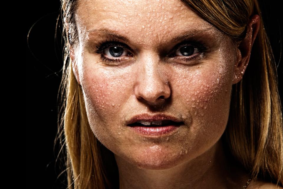 Nærbillede af kvindes ansigt med svedperler i intenst portrætfoto mod mørk baggrund. Stærkt lys og tydelige øjne nuancer.