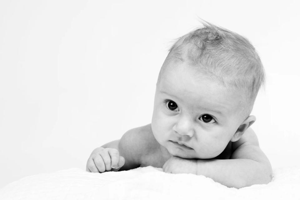 Babyfotografering: Nysgerrigt babyportræt i naturligt lys, baby kigger spørgende fra hvid baggrund.