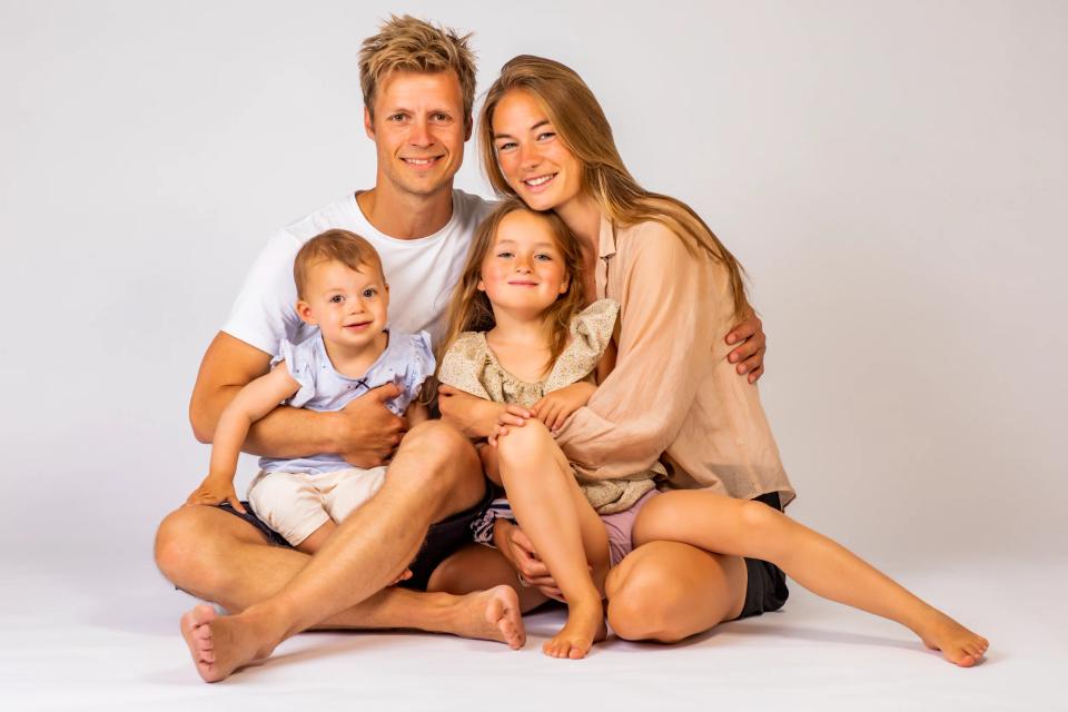 Familie fotografering med far, mor, lille baby og pige der smilende sidder tæt sammen på hvid baggrund.