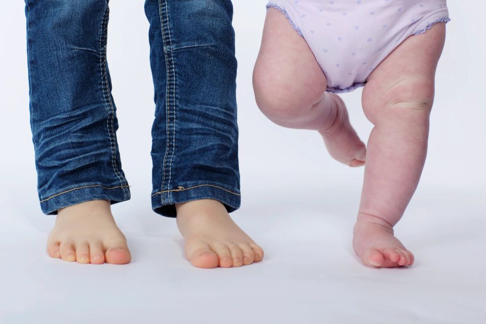 Børnefoto med små bare fødder fra et barn i jeans og en baby i blød lilla ble. Naturligt lys.