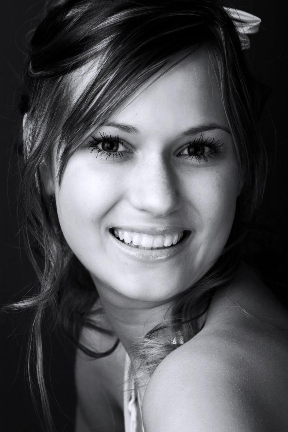 Portrætfoto i sort/hvid af smilende kvinde. Blød belysning fremhæver ansigt og glade udtryk.