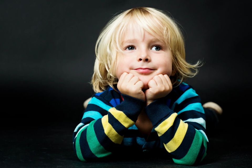 Børnefoto af blond dreng i stribet trøje, der ligger på maven og kigger op med et sødt, betænksomt udtryk.